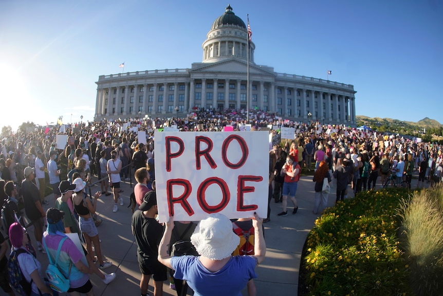 A woman holds a sign that reads "Pro Roe" in front of a large mass of people.