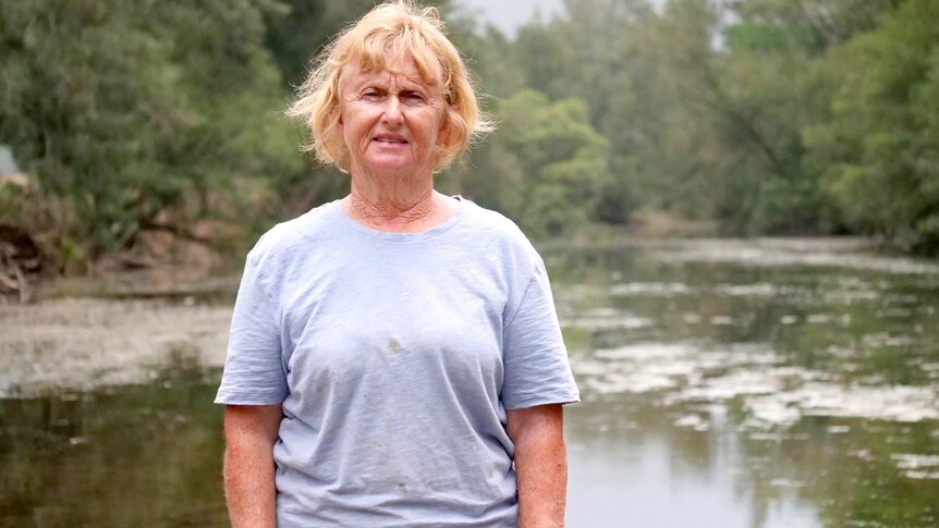 A woman with short dry sandy hair stands in front of the Barrington River.