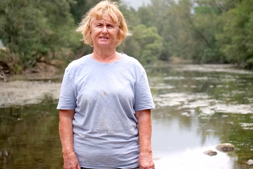 A woman with short dry sandy hair stands in front of the Barrington River.