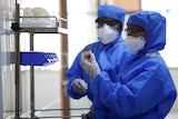 Medical staff in protective clothing handling medicine in a lab.