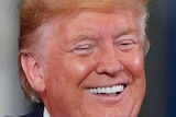 President Donald Trump smiles while speaking at a podium