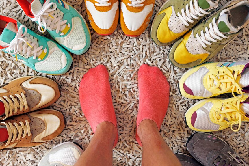 Person's feet surrounded by a circle of running shoes