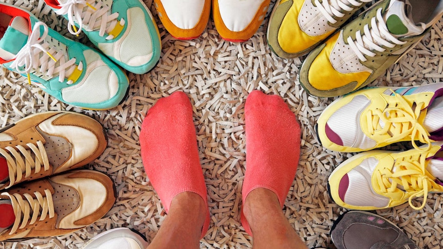 Person's feet surrounded by a circle of running shoes