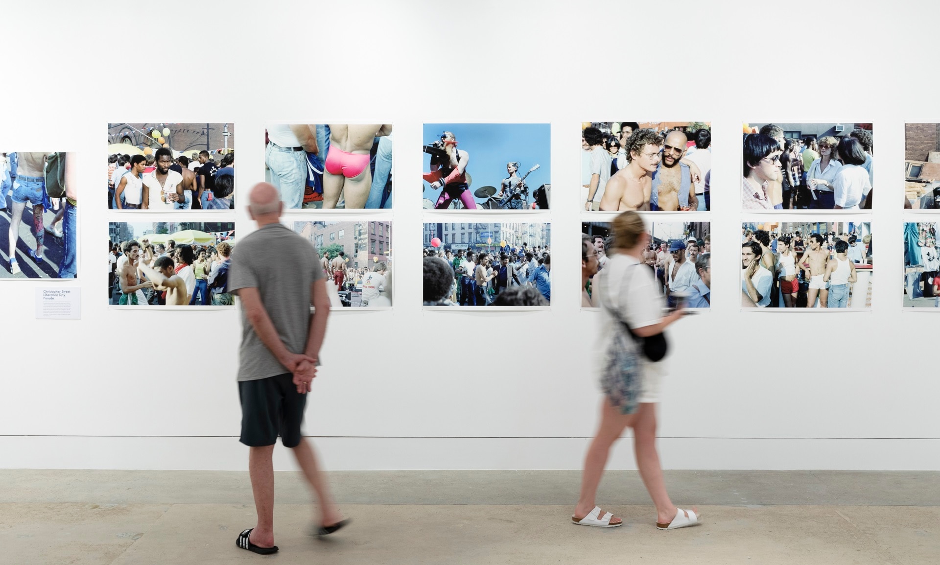 Two people, slightly blurred, stand in front of a series of photographs in a gallery