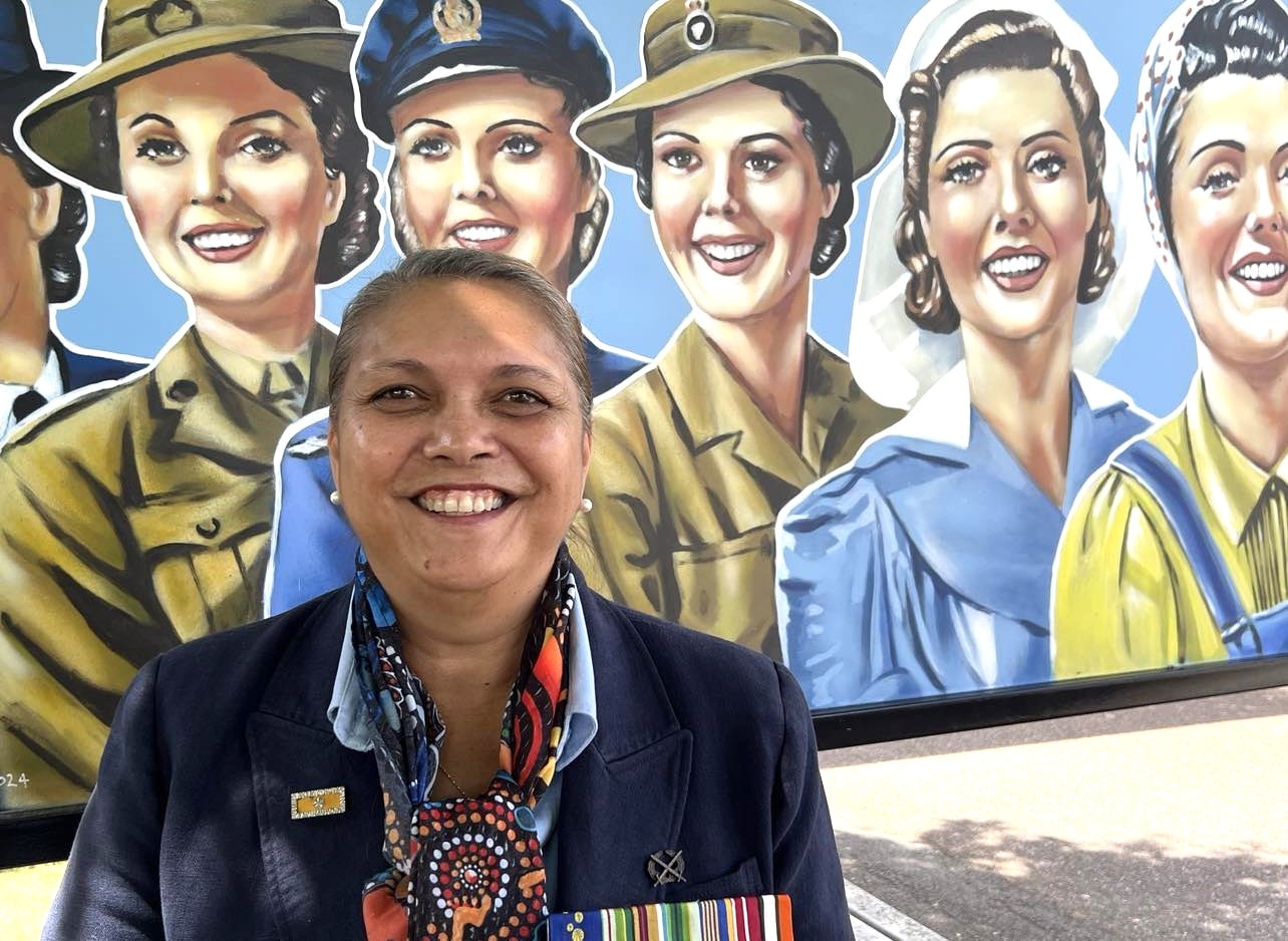 A woman stands in front of a picture with a number of women