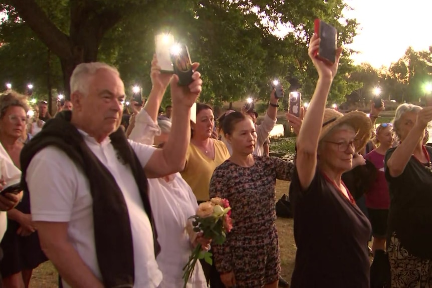 A crowd holding their phones in the air with the phone torches illuminated.