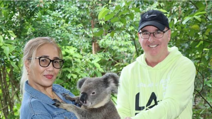 The couple stand holding a koala