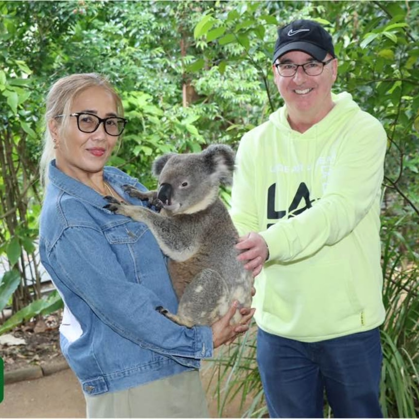 The couple stand holding a koala
