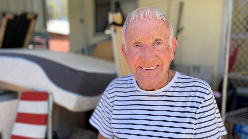 Elderly resident of a caravan park sitting in front of his damaged belongings.