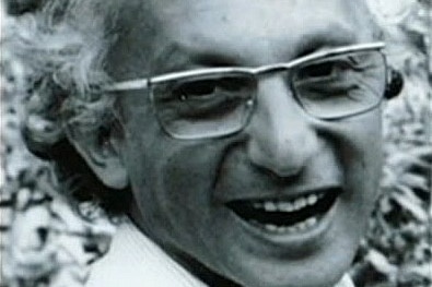 A black and white image of a smiling man wearing glasses.
