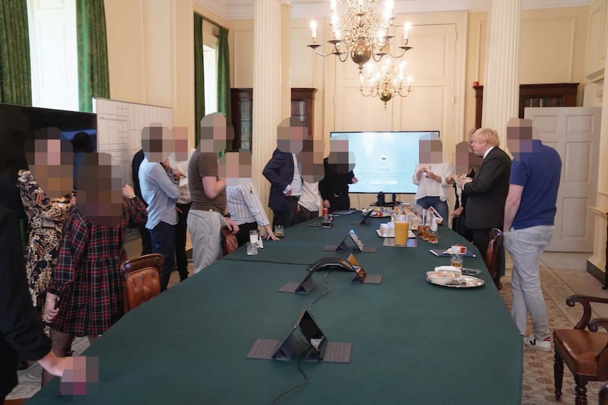 A group of people, all faces blurred but Johnson, stand with drinks around a conference table