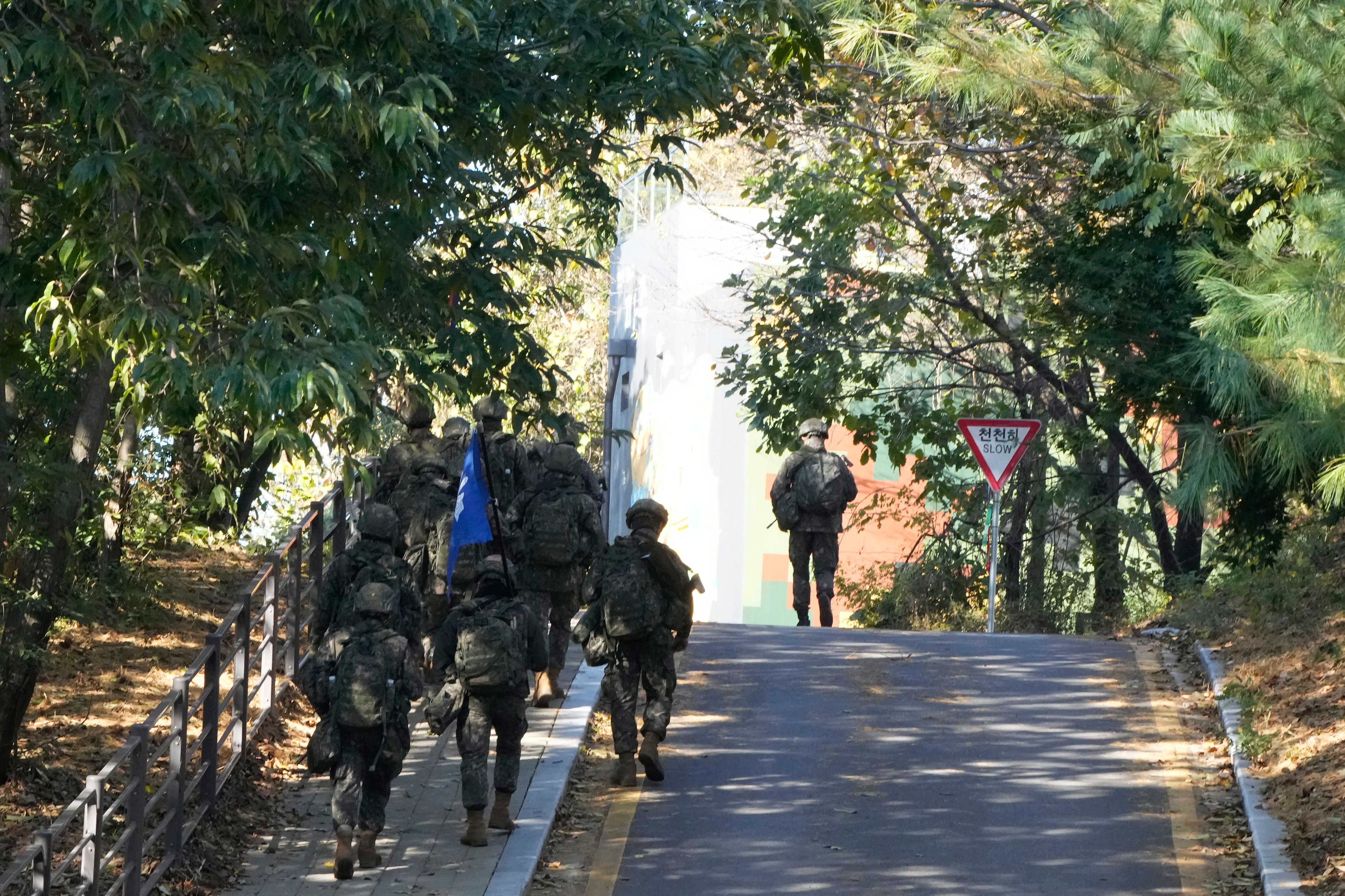 Half a dozen soldiers in uniform walk along a road.