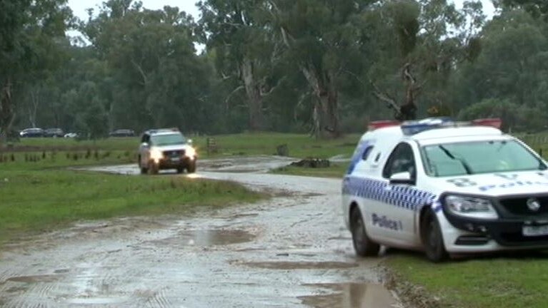 Two police cars driving on a muddy dirt track in a green, rural setting with trees in the background.