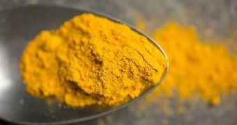 A close up of a teaspoon of bright yellow ground turmeric.