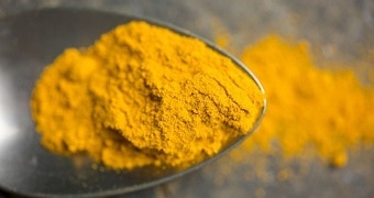 A close up of a teaspoon of bright yellow ground turmeric.