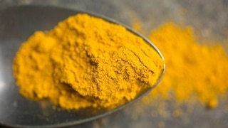 A close up of a teaspoon of bright yellow ground turmeric.
