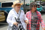 Two women, one with a mobility cane, walk in a carpark.