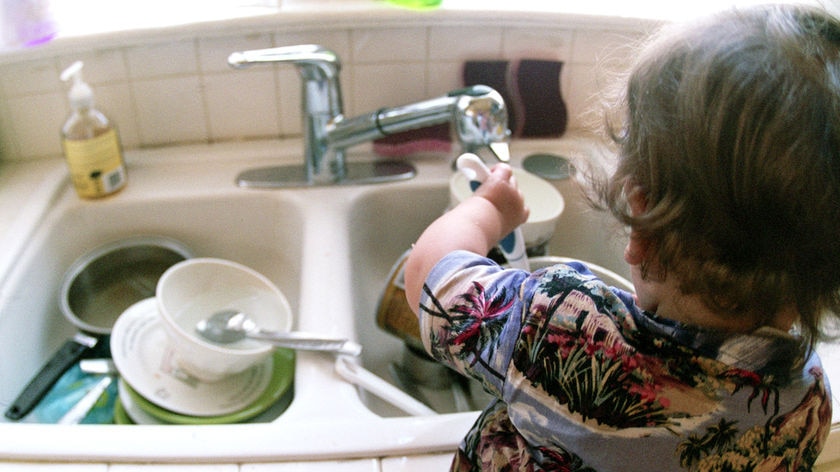 A young boy washes dishes in the kitchen sink