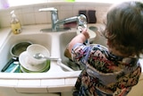 A young boy washes dishes in the kitchen sink.