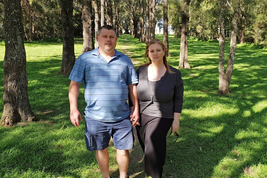 A man and woman hold hands as they walk between rows of trees.