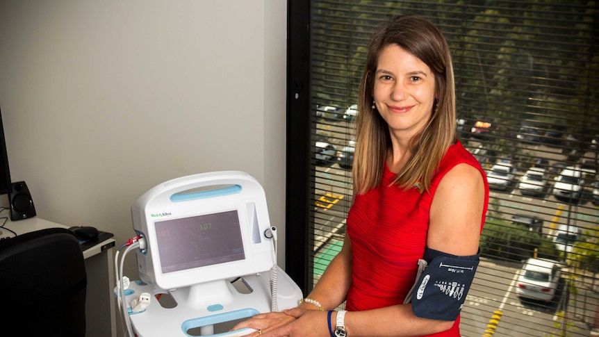 Coralie English stands next to a blood pressure monitor.