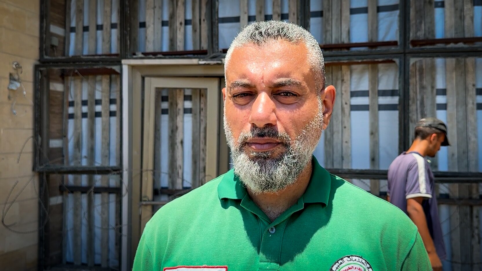 A Palestinian man wearing a green polo out the front of a building.