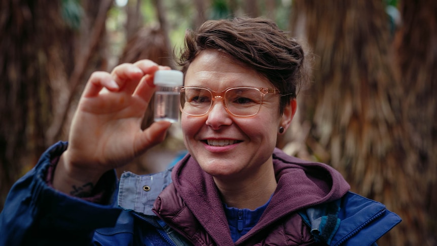 Person in raincoat holds a blastic tube with a tiny insect in it