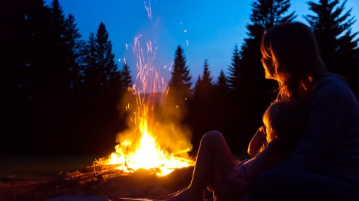 Mother and young child sitting by campfire at night