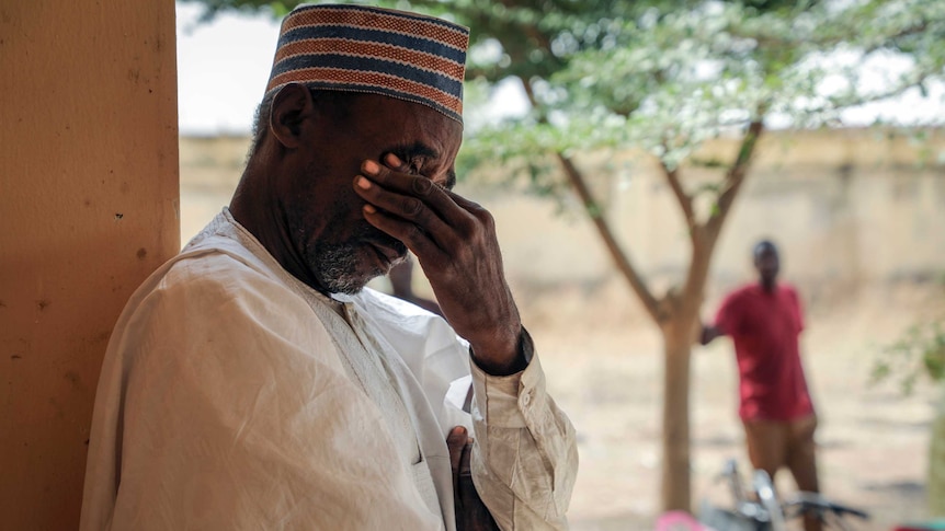 A man places his left hand across his eyes as he leans against a wall.