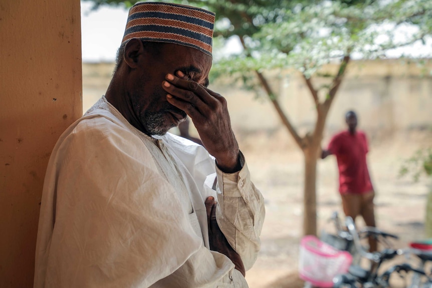 A man places his left hand across his eyes as he leans against a wall.