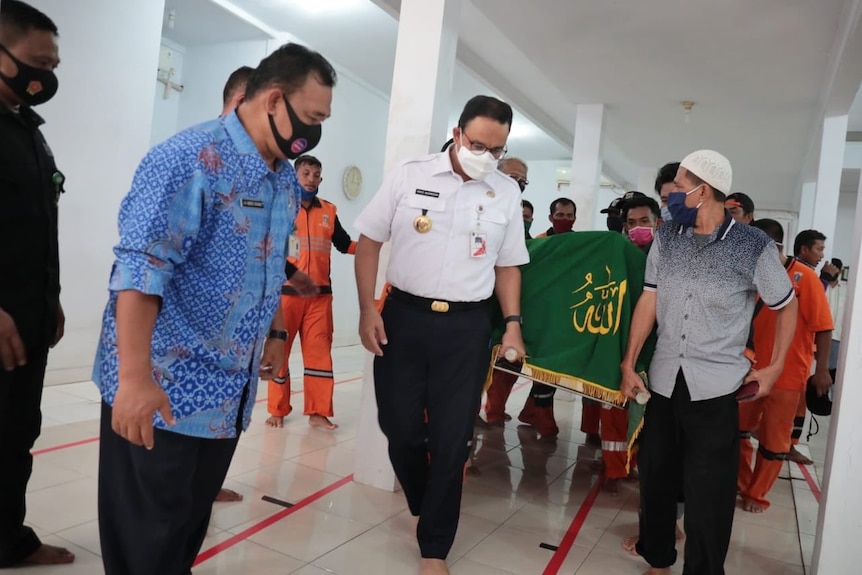 Jakarta Governor Anies Baswedan (centre) wears a mask as he helps carry a coffin.