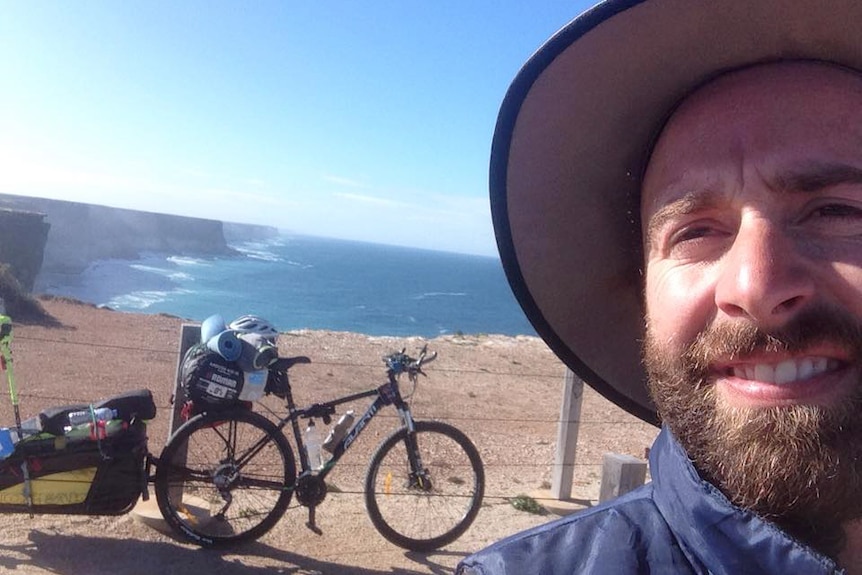 Chris Anderson takes a selfie in front of his bike on the Nullarbor, overlooking the coast.