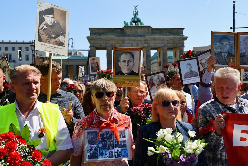 A group of people holding portraits and flowers stand together in a parade.