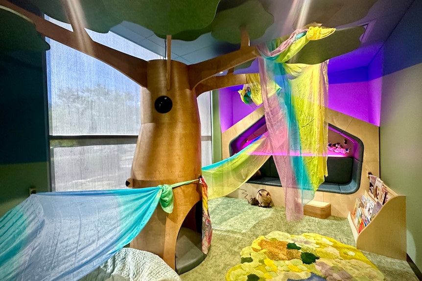 A room with a tree cubby house, reading corner, soft colours and low lighting.