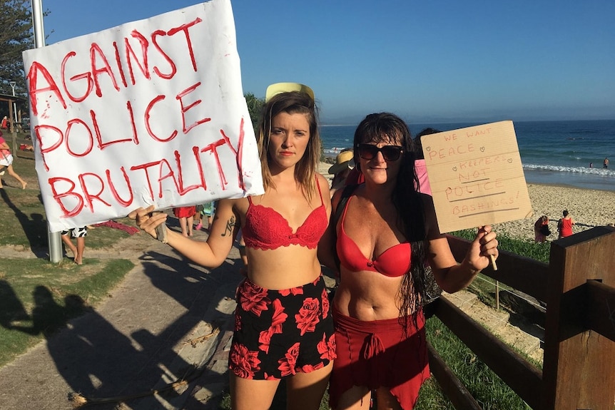 Two women holding signs protesting about police violence in Byron Bay.