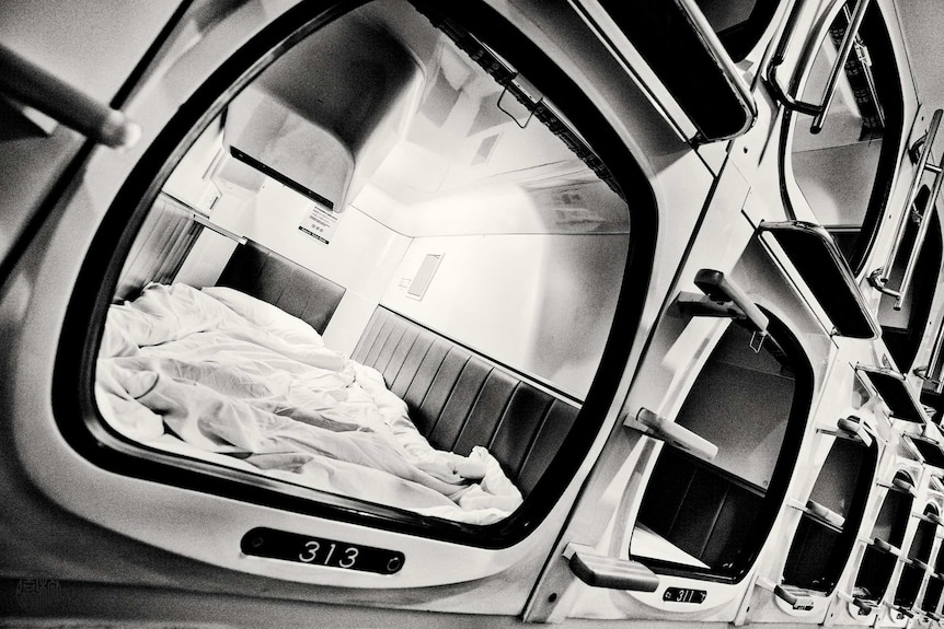 A black and white shot of the capsule interior with messy bed clothes.