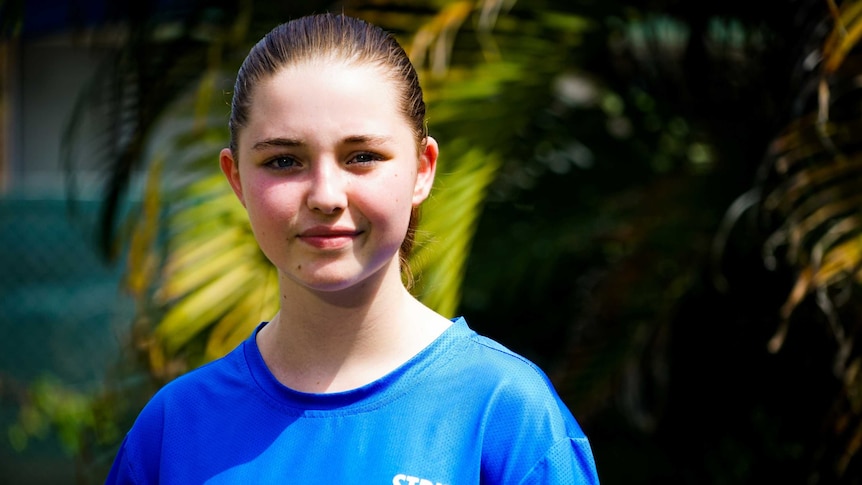 Kaylah is standing outside with a serious expression. Her hair is pulled back and she's wearing a blue shirt.