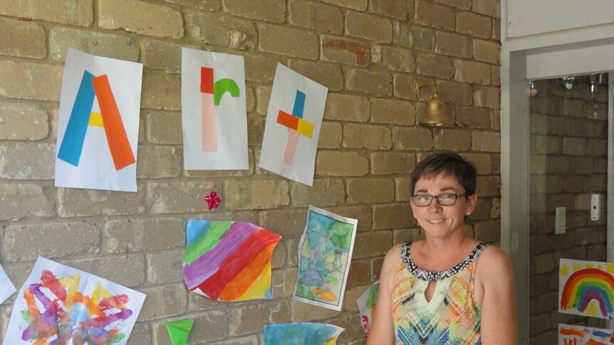 Woman standing in front of children's artworks taped to brick wall