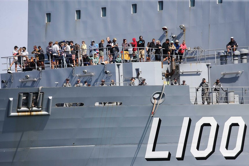 Evacuees standing on an outdoor deck on board the HMAS Choules as it arrives in port.