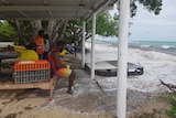 A group of Torres Strait Islander men watch as rising waters lap at their feet.