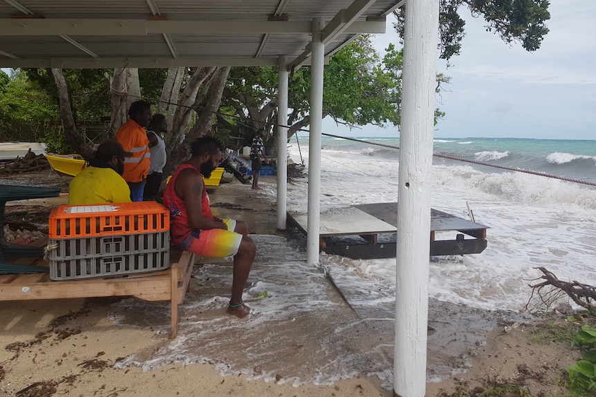 Torres Strait Islander men watch as rising waters lap at their feet.