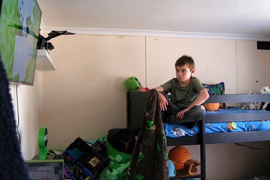 A young boy sits on top of a bunk bed