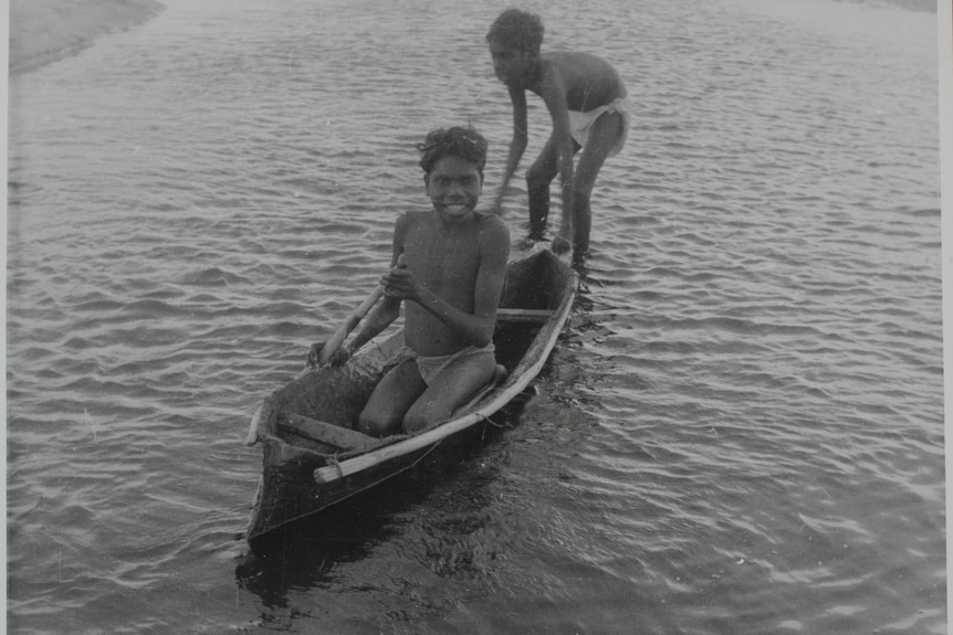 Two Indigenous boys paying with a canoe.