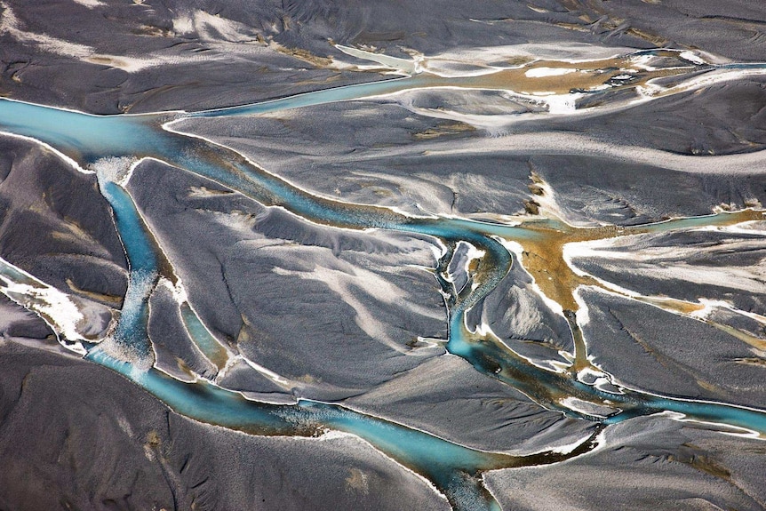 An aerial view of pale blue rivers against grey earth