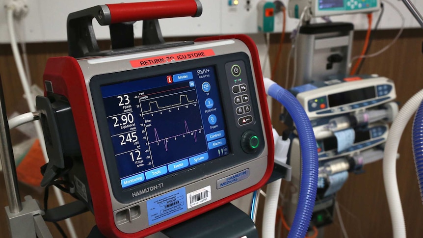 A close-up shot of a ventilator monitor in a hospital room with other equipment along side it.
