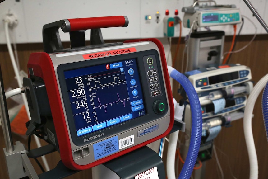 A close-up shot of a ventilator monitor in a hospital room with other equipment along side it.