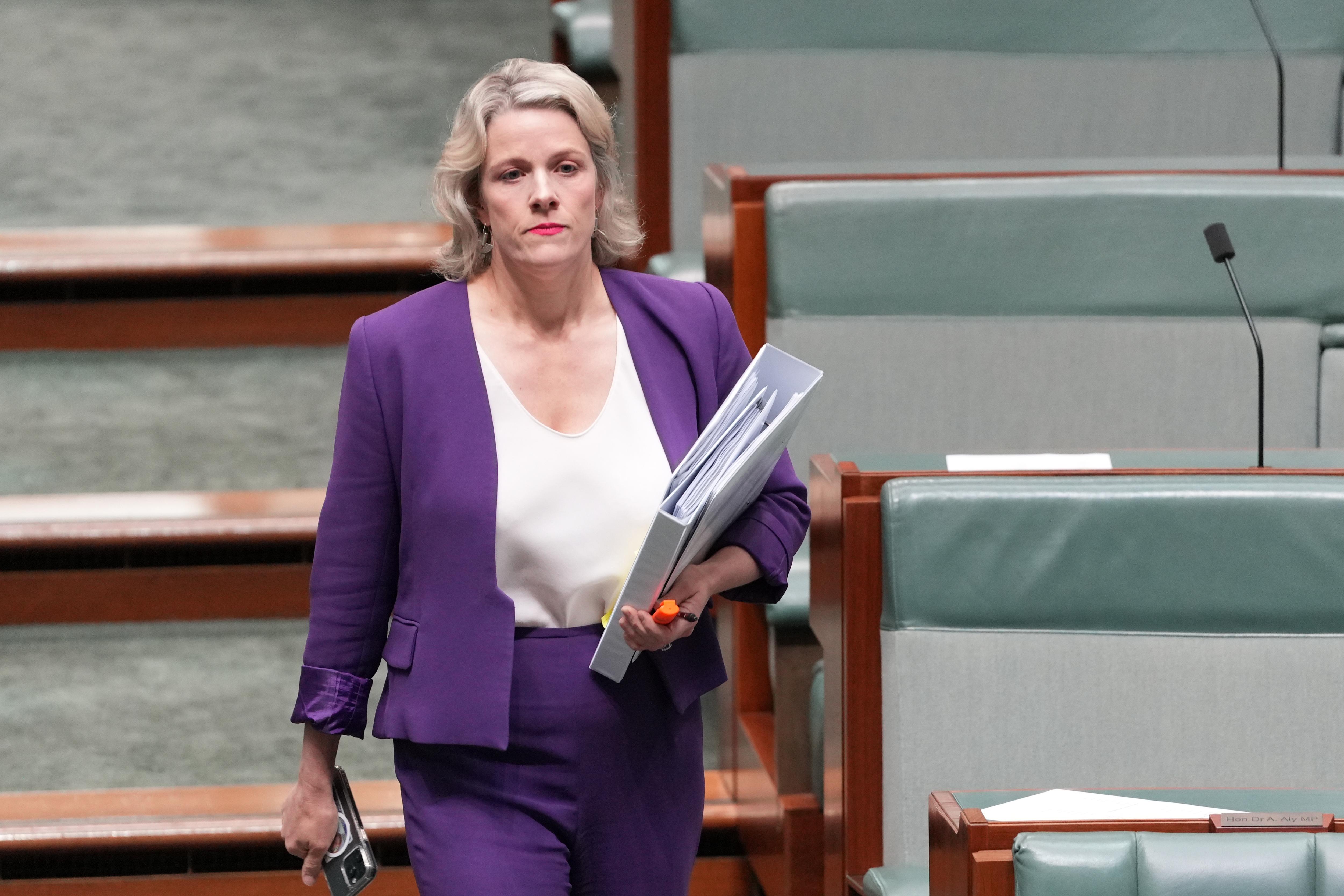 Una mujer vestida con chaqueta y pantalón morado sosteniendo carpetas.
