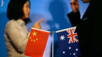 Two people talk in front of the Chinese and Australian flags.