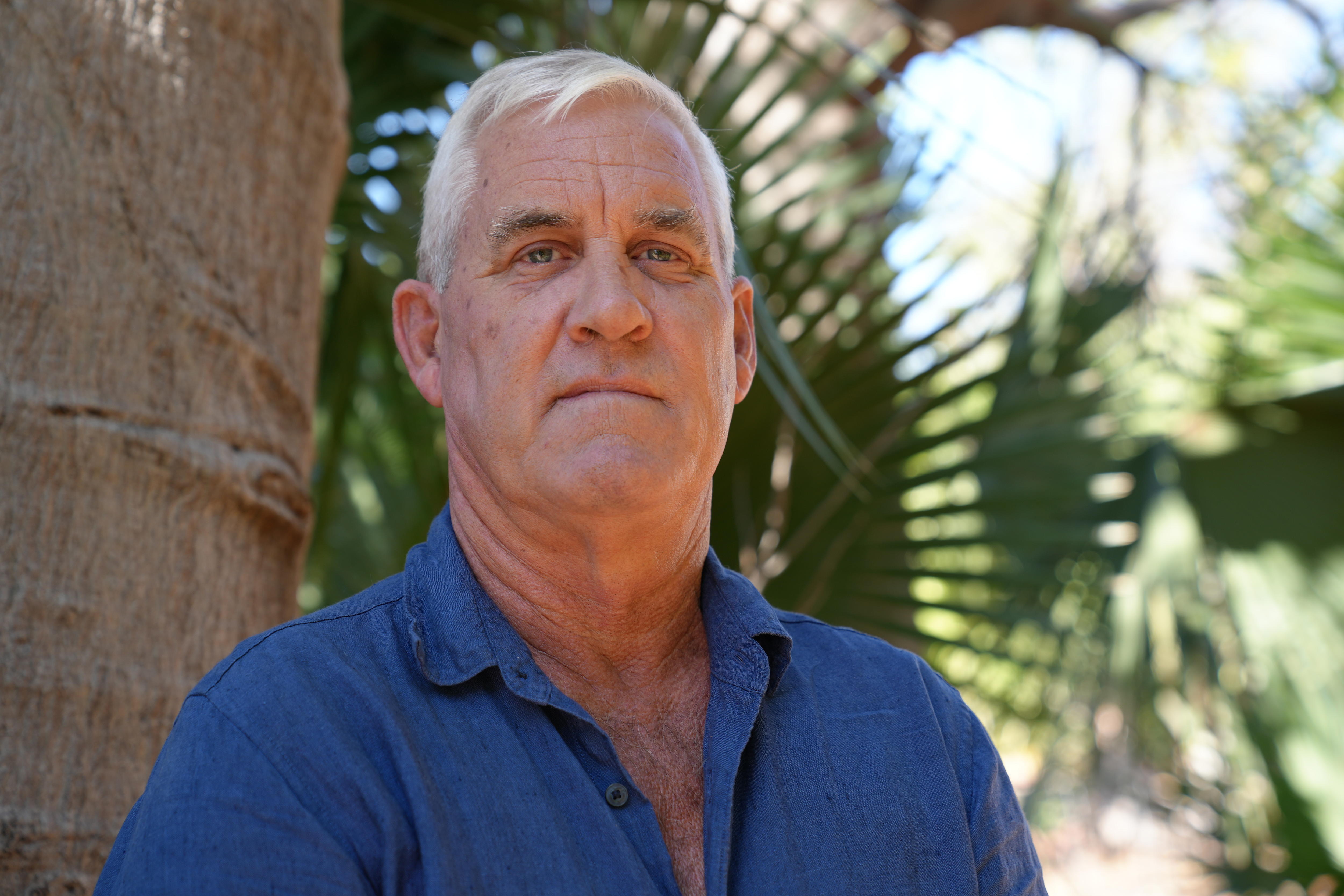 Hombre con cabello blanco y ojos azules posando cerca de un árbol de boab.