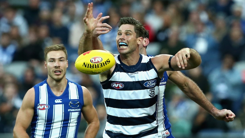 A Geelong AFL player tries to catch the ball in front of a North Melbourne opponent.